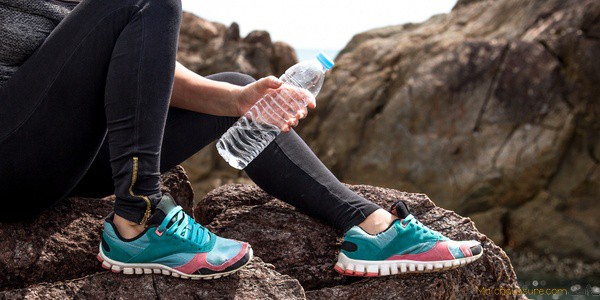 Femme qui porte une paire de chaussures d'alpinisme et qui tient une bouteille d'eau